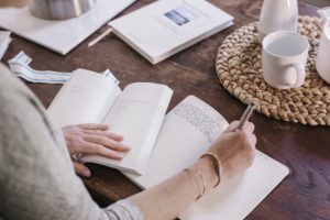 Woman sitting at a table in her apartment, writing in a diary, morning routine.