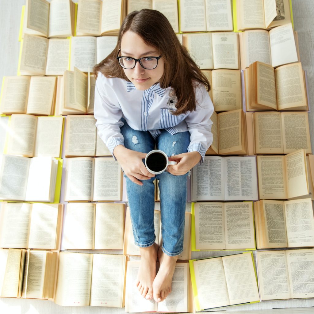 Young happy girl reading a book and drinking coffee. View from above. Concept for World Book Day.
